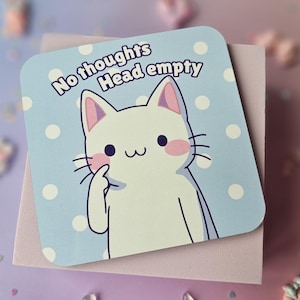 May include: Square sticker with a white cat illustration, pink details, and a light blue polka dot background. The text "No thoughts Head empty" is printed above the cat. The sticker is placed on a pink surface.