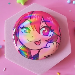 May include: A round, holographic sticker featuring a colorful anime-style character with pink hair and a playful expression. The sticker is placed on a pink hexagonal base, surrounded by star-shaped and spherical decorations on a pink background.