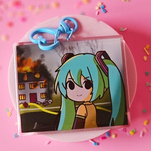 Llavero acrílico con impresión de doble cara con meme de Miku Disaster Girl y acabado epoxi completo