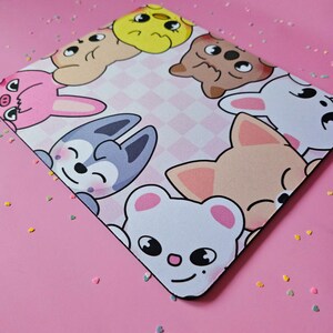 May include: A pink and white mouse mat with a checkered pattern and cartoon animal faces. The animals include a chick, a fox, a cat, a dog, and a bear.