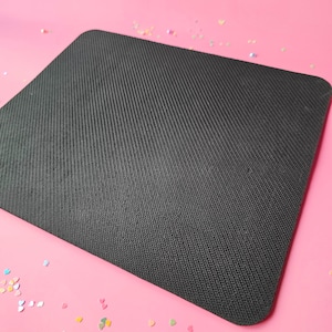 May include: A black mouse mat with a textured surface. The mouse mat is on a pink background.