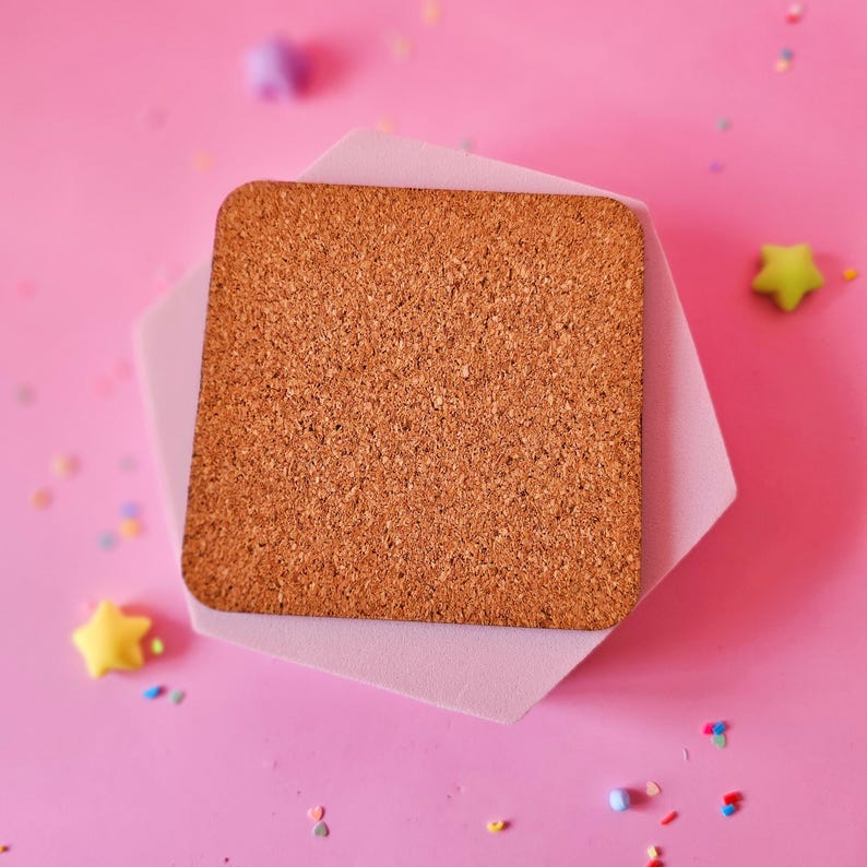 May include: A square cork coaster with a natural brown color sits atop a light pink hexagonal coaster. The background is a vibrant pink, with scattered star-shaped and confetti-like decorations.