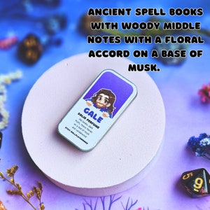 K&ouml;nnte beinhalten: Eine kleine, runde, silberne Dose mit einem violetten Etikett, auf dem "GALE SOLID PERFUME" steht. Auf dem Etikett ist eine Comic-Illustration einer Person mit braunen Haaren und einem blauen Hemd zu sehen. Der Text auf dem Etikett lautet "Old books, dark fruits, heavy florals on a bed of musk and sandalwood."