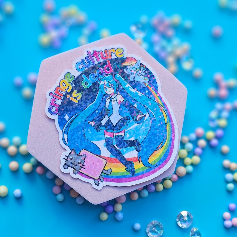 May include: A pink and blue sticker with a rainbow background and the text "Cringe Culture is Dead". The sticker features a cartoon anime character with blue hair and a pink and blue outfit. The character is holding a pink and white cat.