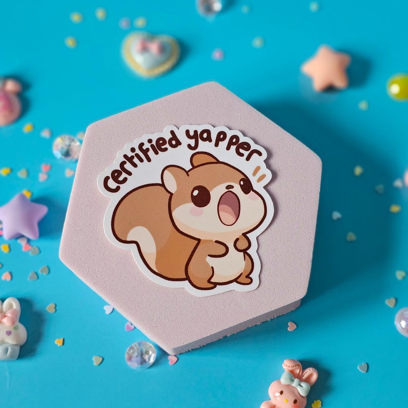May include: A pink hexagonal sticker featuring a cartoon squirrel with brown fur and a white belly. The squirrel is shouting and has the text "Certified yapper!" above it.