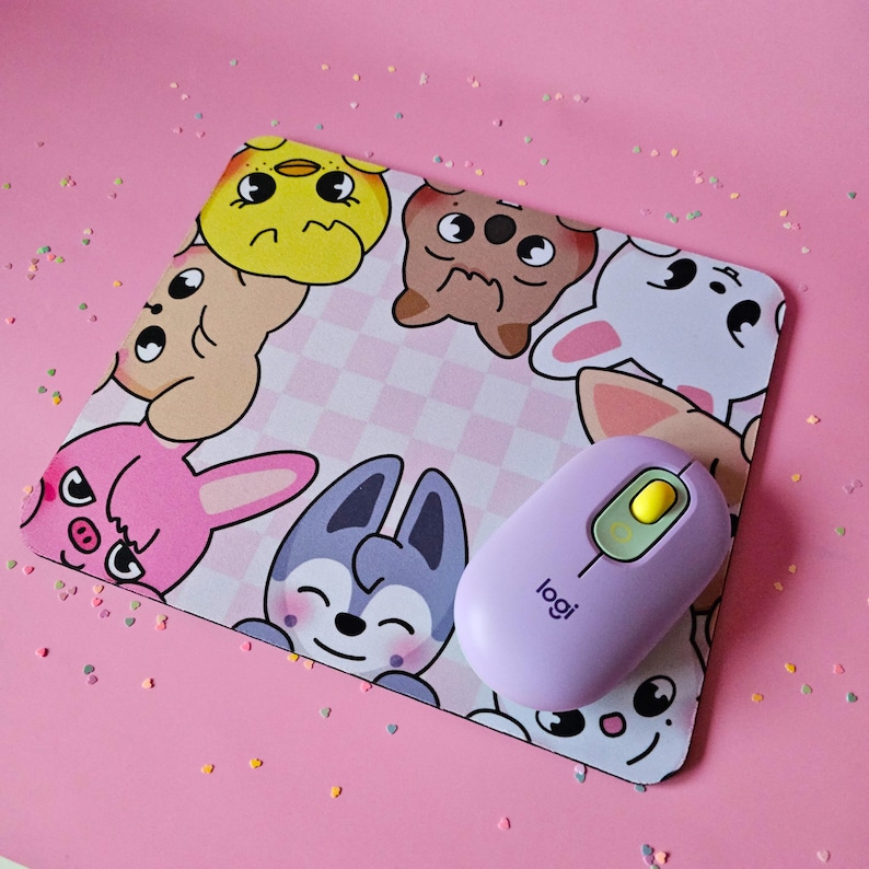 May include: A pink and white mouse mat with a checkered pattern and cartoon animal illustrations. A purple wireless mouse with a yellow button is on top of the mouse mat. The mouse mat has the text "logi" on it.