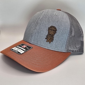 May include: A gray and brown baseball cap with a mesh back. The front of the cap features a brown pineapple graphic with the text "LYKK" on it. The cap is adjustable and has a Richardson brand label.