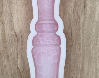 May include: A pink silicone mold in the shape of a vase. The interior of the vase has a pattern of irregular shapes. The mold is outlined in white and sits on a wooden surface. The mold is designed for crafting.