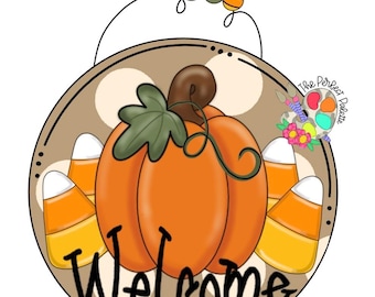 May include: A round wooden door sign featuring a central orange pumpkin with a green leaf and brown stem, flanked by candy corn. The background is tan with white polka dots. The word Welcome is written in black script. Includes a wire hanger with beads.
