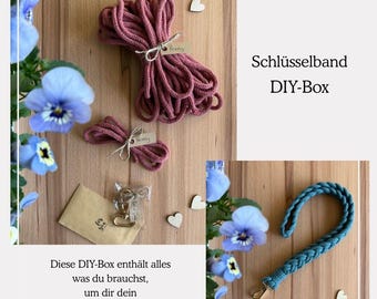 May include: A DIY kit for making a key chain. The kit includes a spool of pink cord, a small spool of pink cord, a metal key ring, and a small envelope. The text on the image reads "Diese DIY-Box enthält alles was du brauchst, um dir dein eigenes Schlüsselband in Wunschfarben anzufertigen!" and "Schlüsselband DIY-Box".