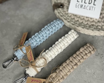 May include: Three keychains made of knotted rope in blue, white, and brown. Each keychain has a silver key ring and a small tag with the word "Natur" or "Sound" written on it. The background is a light gray surface.