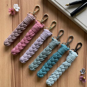 May include: Six braided keychains in various colors, including pink, purple, green, and blue. The keychains have gold and silver clasps.