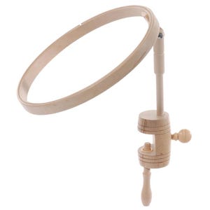 Peut inclure: Un tambour à broder en bois clair fixé sur un support vertical réglable. Le support comprend un mécanisme de serrage circulaire avec une vis en bois pour fixer l'appareil sur une surface plane, permettant de réaliser des projets de broderie.