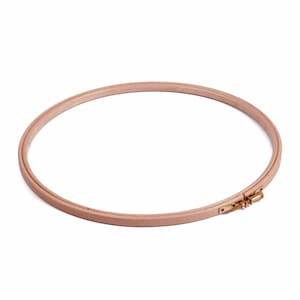 Puede incluir: Un bastidor de bordado circular fabricado en madera de tono claro, con un acabado liso y un mecanismo de tornillo de ajuste de tensión metálico en color latón, diseñado para mantener la tela tensa para labores y diversos proyectos de manualidades.