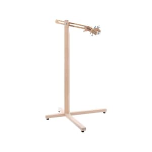 May include: A light-colored wooden floor stand featuring a vertical post supported by a cross-shaped base with small black feet. An adjustable horizontal arm extends from the top, equipped with a metal clamp mechanism for securing items.