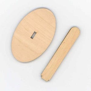 Könnte beinhalten: Zwei unfertige Holzstücke. Eines ist oval mit einem rechteckigen Schlitz in der Mitte. Das andere ist ein langes, schmales Rechteck mit abgerundeter Oberseite und gekerbtem Boden. Beide Teile sind hellbraun.