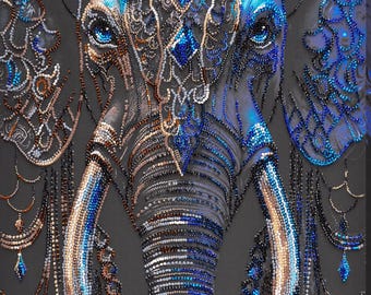 Op de afbeelding: Close-up van de kop van een olifant gemaakt van blauwe, zilveren en gouden kralen. De ogen van de olifant zijn groot en blauw, en zijn slurf is lang en gedetailleerd.