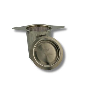 May include: Stainless steel tea infuser with a mesh basket and a matching saucer. The infuser has a handle on each side for easy handling. The saucer has the words "Vegan Elephant" printed on it.