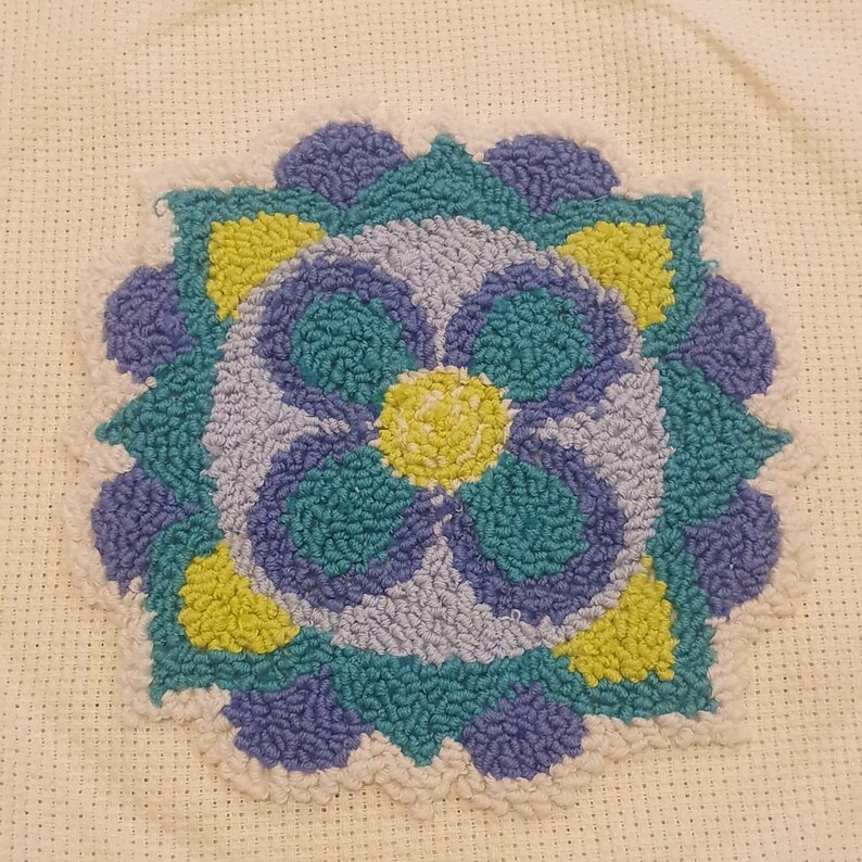 K&ouml;nnte beinhalten: Nahaufnahme eines bunten, handgen&auml;hten Teppichs mit floralem Muster. Der Teppich ist aus verschiedenen Farben gefertigt, darunter Blau, Gr&uuml;n und Gelb.