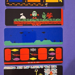 May include: Five rectangular stickers with retro video game graphics. The designs include pixelated images of a key, a treasure chest, a character, a monster, and a level with the word "HELD" in a classic font.