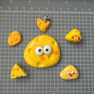 Op de afbeelding: Een verzameling gele kaasvormige objecten met cartoongezichten en een kleine grijze muis op een stukje kaas. De kaasstukken hebben gaten en zijn gerangschikt op een grijs rasteroppervlak.