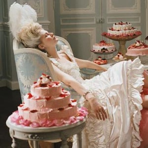 May include: A scene depicting a woman in a white gown reclining on a chaise lounge, surrounded by cakes. A maid is attending to her feet. The cakes are tiered and decorated with fruit and flowers, suggesting a theme of luxury and indulgence.