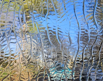 May include: A close-up of a textured glass surface with a blue sky and green trees reflected in the glass.