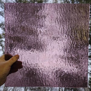 May include: A sheet of textured glass with a light purple hue. The glass has a rippled, wave-like pattern.