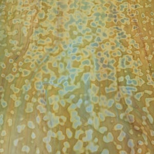 May include: A sheet of glass featuring a mottled pattern of soft amber, tan, and pale blue organic shapes. The surface displays a smooth, semi-translucent texture with blended color transitions that create a fluid, marbled appearance throughout.