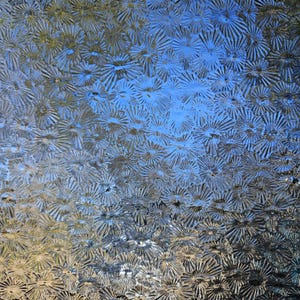 May include: Close-up of textured glass with a repeating pattern of starburst shapes. The glass has a frosted appearance with a mix of blue, silver, and gold tones, creating a shimmering effect. The background is a gradient of blue and gold.