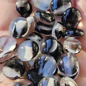 May include: A collection of glass marbles with a swirl design in black, white, and clear. The marbles are oval and round, with a glossy finish. The marbles are a decorative item.