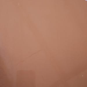 May include: A solid, muted orange-brown background with a subtle, irregular crack running diagonally across the surface. The color is uniform, with no visible patterns or textures.