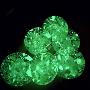 May include: A collection of six glowing green, circular coasters. Each coaster has a speckled, textured appearance, with a mix of light and dark green hues. The coasters are arranged against a dark background, creating a striking contrast.