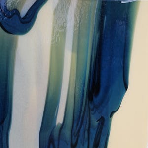May include: A smooth, glossy surface featuring vertical, flowing streaks of deep navy blue and translucent teal layered over a solid, pale cream-colored background. The colors blend in elongated, organic shapes with a reflective finish.