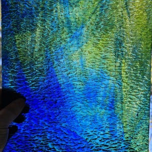 May include: A rectangular piece of textured glass with a gradient of colors. The top right corner is green, transitioning to blue and then a deep blue at the bottom. The glass has a rippled surface.