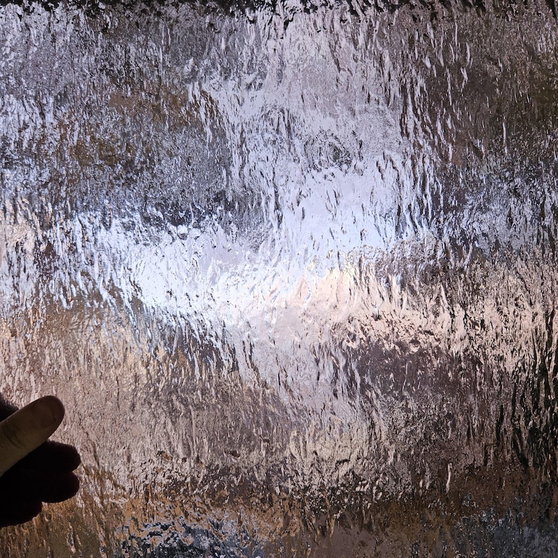 May include: A close-up of a textured glass surface with a rippled pattern. The glass is translucent and reflects light, creating a shimmering effect.