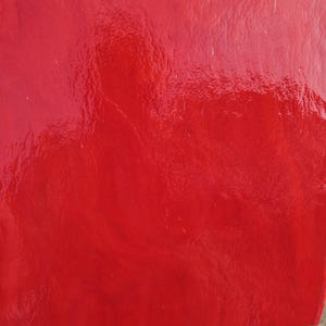 May include: A close-up of a glossy, red surface. The surface has a textured appearance with subtle variations in color and highlights. The overall effect is a vibrant, eye-catching design.