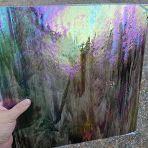 May include: A square sheet of iridescent stained glass featuring a swirling pattern of dark gray, black, and deep green tones. The surface has a reflective, metallic sheen that shifts between vibrant purple, blue, and gold highlights.