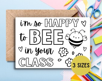 May include: Black and white printable card with the text "i'm so happy to BEE in your CLASS" and a cartoon bee with a heart. The card also has flowers and hearts. The text "3 SIZES" is in a yellow circle.