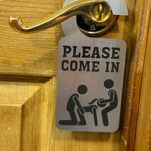 May include: A silver door hanger with the text "PLEASE COME IN" and a black silhouette of two people.