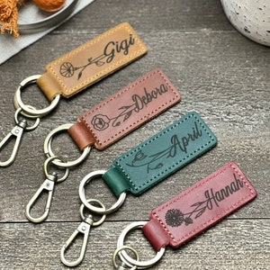 Op de afbeelding: Vier gepersonaliseerde leren sleutelhangers met bloemenmotieven en de gegraveerde namen Gigi, Debora, April en Hannah.