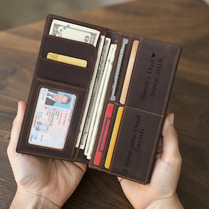 May include: Open brown leather wallet filled with cash, credit cards, and an ID card. The wallet has the text "Sarah's Dad Since 2018" and "I love you Dad - Sarah" engraved on it.