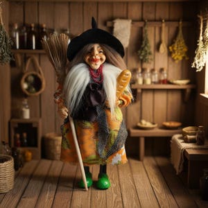 Könnte beinhalten: Puppe einer Hexe mit schwarzem Hut, die einen Besen und ein Brot hält. Die Hexe hat einen weißen Bart, eine rote Halskette und ein orange-grünes gemustertes Kleid. Sie trägt grüne Schuhe.