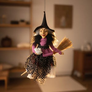 Può includere: Decorazione di Halloween con una bambola a forma di strega sospesa. La strega indossa un cappello a punta nero, un top rosa e una gonna a pois bianchi e neri. Tiene in mano una borsa bianca e cavalca una scopa, creando un'atmosfera festosa e spettrale.
