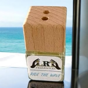 Può includere: Una bottiglia di diffusore in legno con un contenitore in vetro trasparente e un'etichetta che recita "LRH Fragrances Ride the Wave".