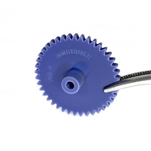 Puede incluir: Primer plano de un engranaje de plástico azul con muchos dientes, sujetado por unas pinzas sobre un fondo blanco. El engranaje tiene un cubo central y el texto "FOTOTELEKTRIK PL" y "F 8222-41".