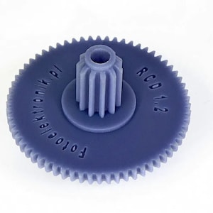 Puede incluir: Un engranaje de plástico azul con el texto "Fotoelektronik.pl" y "RCD 1:2" impreso en él.