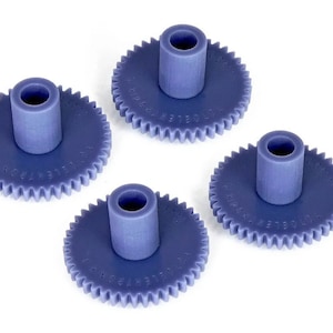 Puede incluir: Cuatro engranajes de plástico morado con un agujero central. Cada engranaje tiene una serie de dientes alrededor del borde exterior.