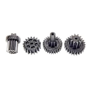 May include: Four small black plastic gears with teeth. The gears are arranged in a row, with the largest gear on the left and the smallest gear on the right.