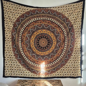 Könnte beinhalten: Ein großes, rechteckiges Wandtuch mit einem detaillierten Mandala-Design in Braun-, Orange- und Schwarztönen. Das zentrale kreisförmige Muster ist von komplizierten geometrischen und floralen Motiven umgeben. Das Wandtuch hat einen schwarzen Rand.
